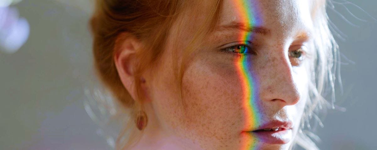 A young woman’s profile with a prism of rainbow light shining on her face.