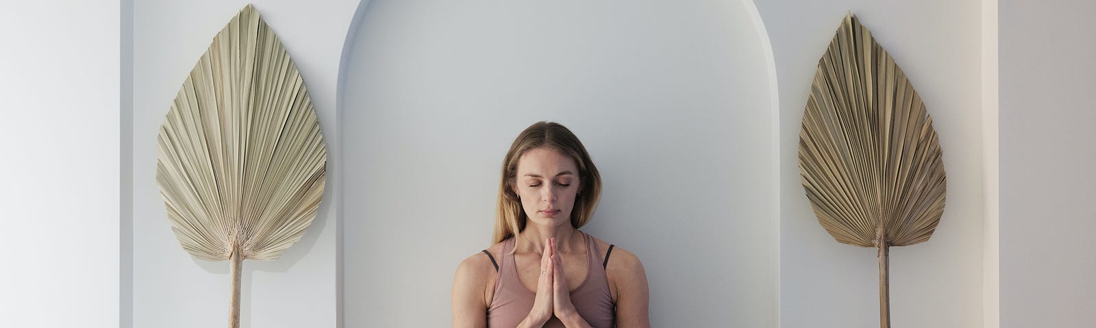 A woman in meditation dressed in muted sports attire with her eyes closed and her hands in a prayer shape.