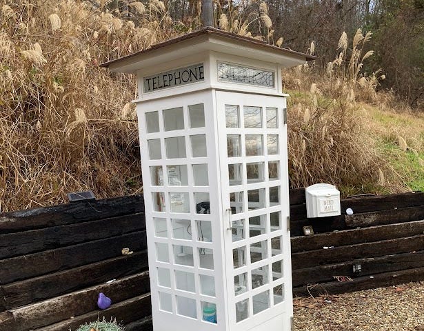 White wood and glass phone booth in a garden.