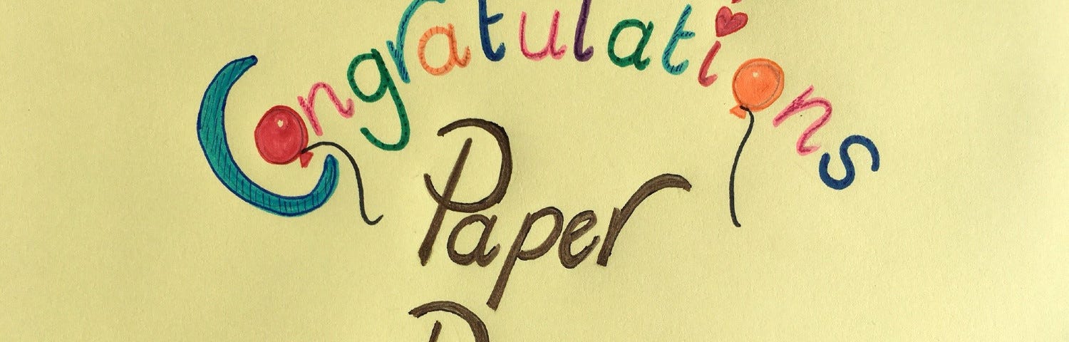 A yellow poster with colorful handwritten words, ‘Congratulations Paper Poetry’ embellished with balloons and hearts.