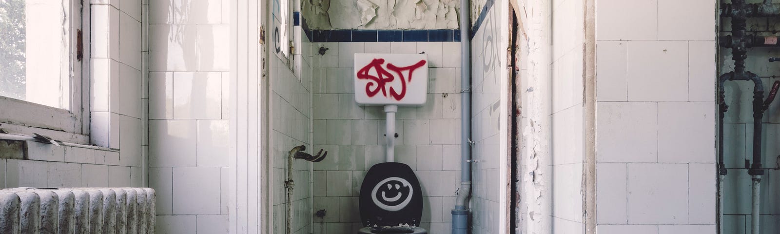 A white bathroom with dirty walls with a smiley face painted on the toilet lid