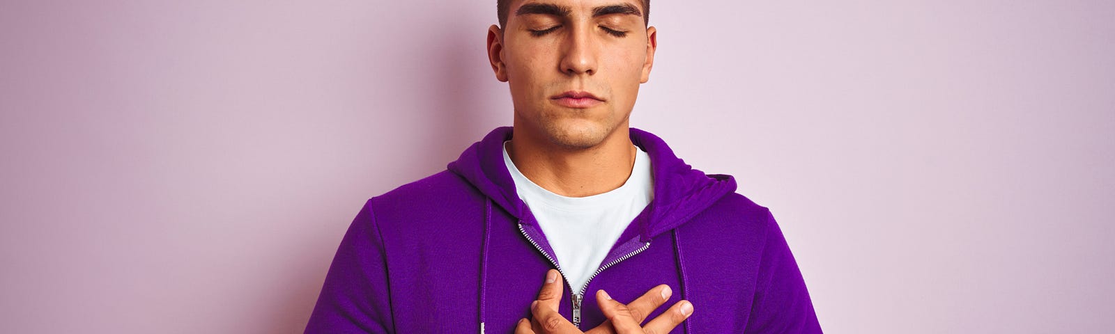 Young handsome man wearing purple sweatshirt over pink isolated background smiling with hands on chest with closed eyes