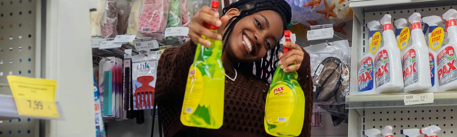 Black girl in supermarket holding up two bottles of yellow spray