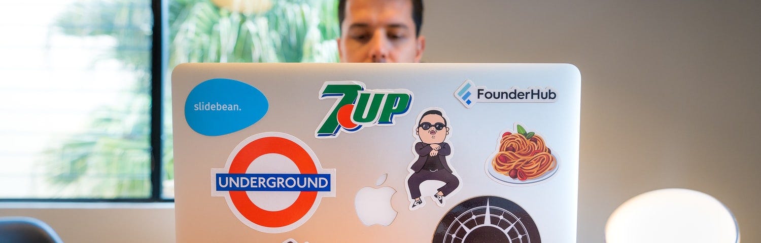 Man sitting at laptop filled with logos on the back.