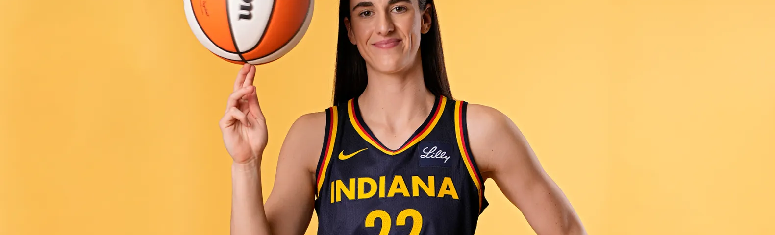 Photo of Caitlin Clark in her Indiana Fever jersey and twirling a orange and white basketball on her right middle and index fingers.