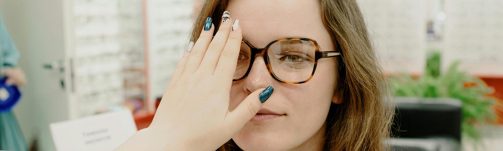 An optician covering an eye of a woman with long brown hair.