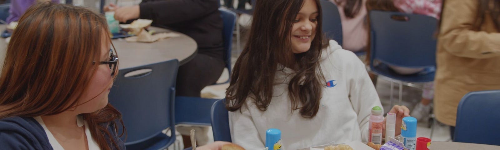 Two students sit at a table with lunch trays.