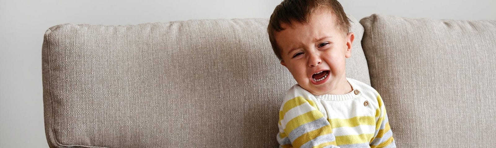 crying toddler sitting on couch