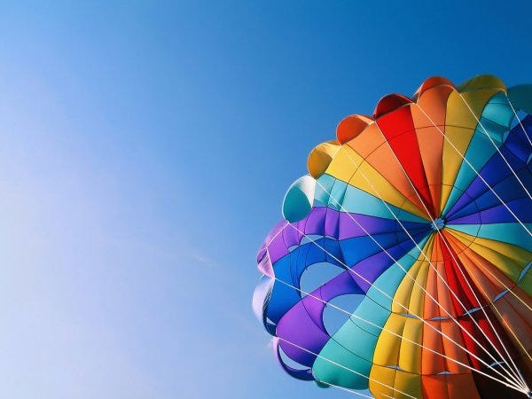 Imagem da cúpula de um paraquedas colorido contra um fundo de céu azul