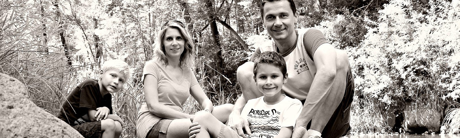 Back and white photo of a family of four sat on rock by the river.