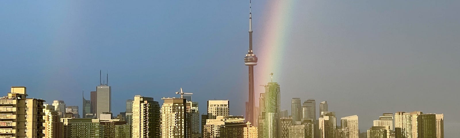 Skyline of Toronto with the CN Tower in the middle and a bright rainbow coming down in front of the Tower