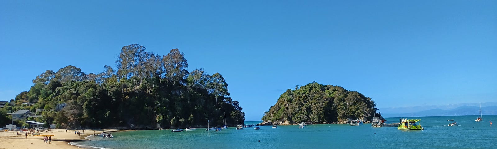 Yellow sand, calm blue water dotted with boats, NZ beach.