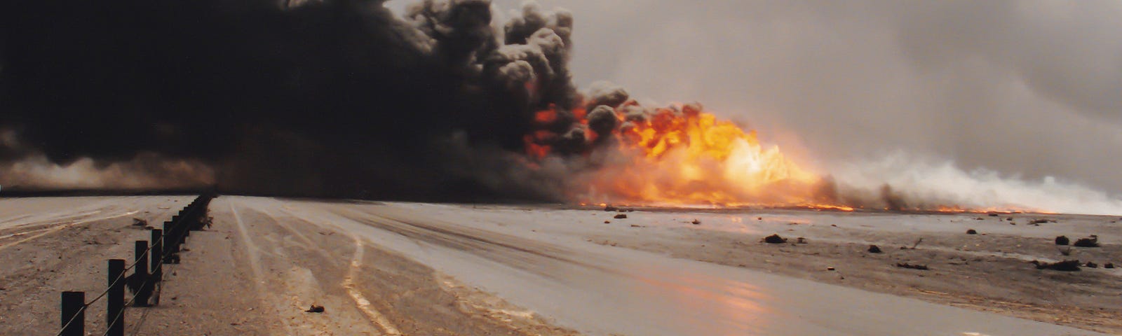 Road with fire raging in the distance and smoke blowing over the asphalt