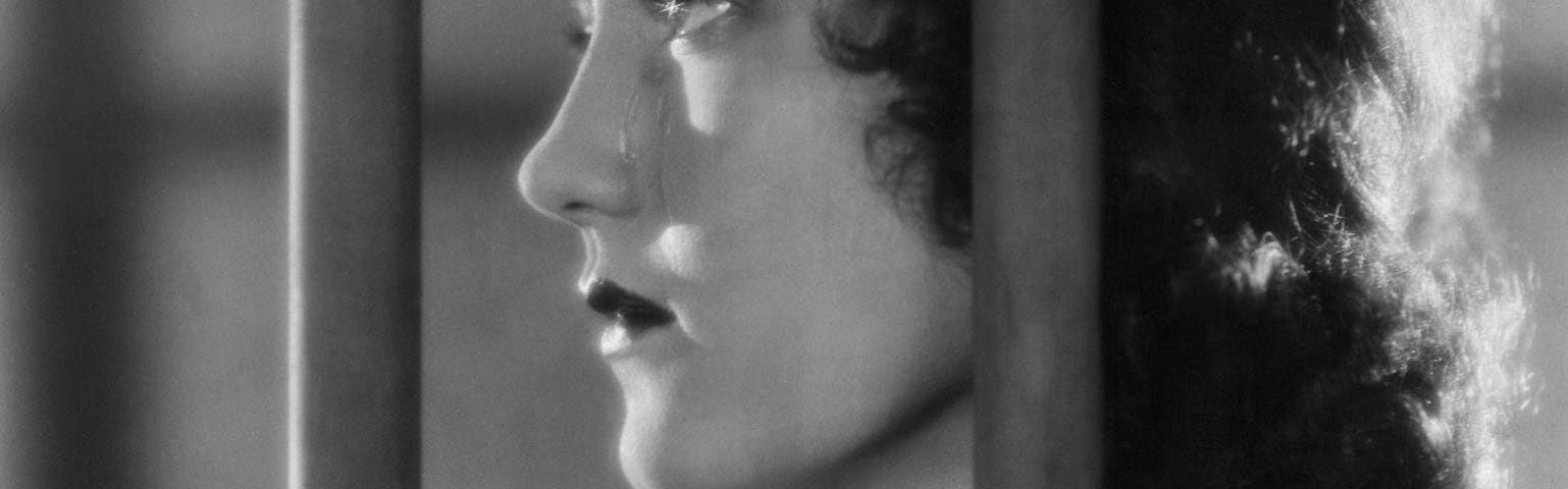 A woman behind bars looks out into the distance from her jail cell.