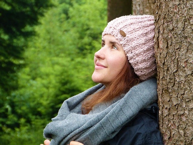 Photo of a young woman leaning against a tree trunk smiling and looking up.