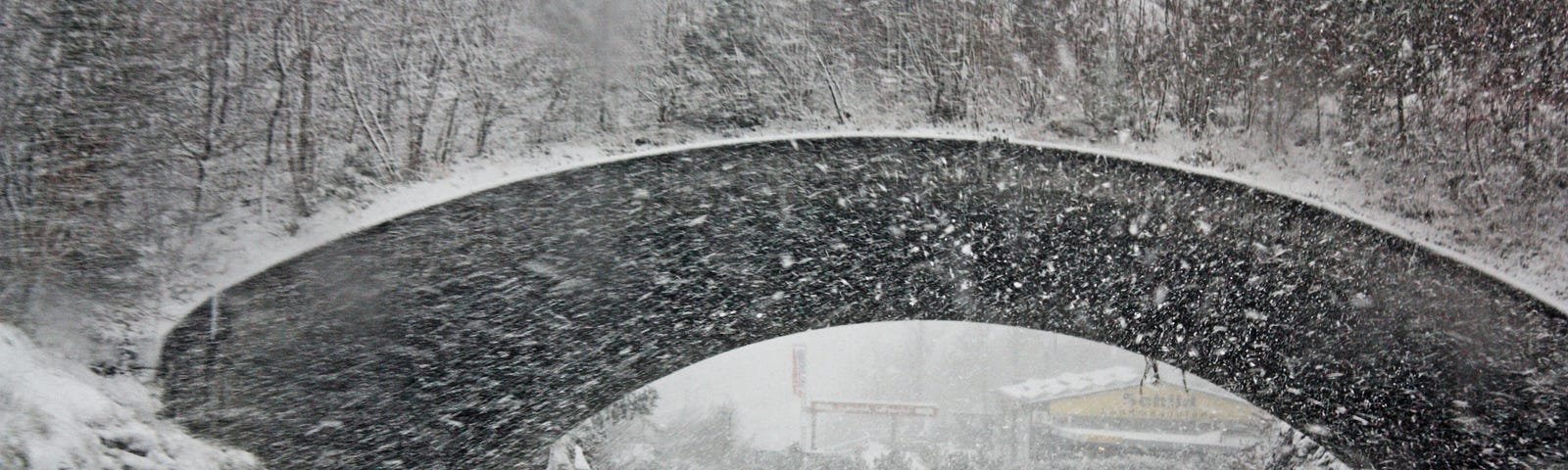 Car on snowy road, driving beneath bridge