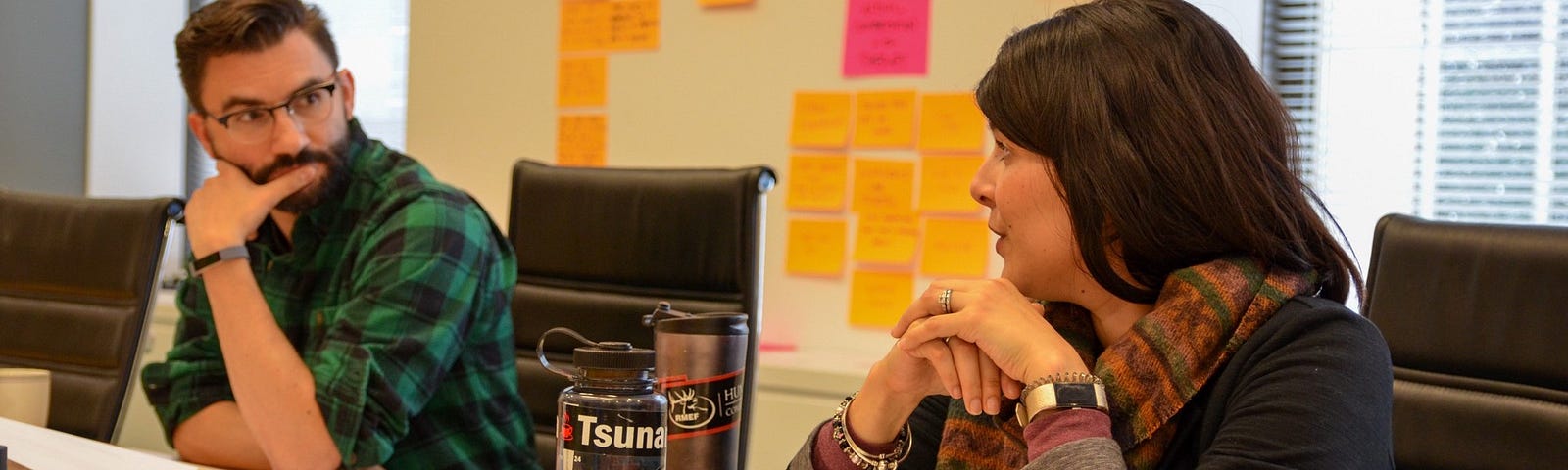 Two researchers consult with each other. The table & walls around them are covered with sticky notes.