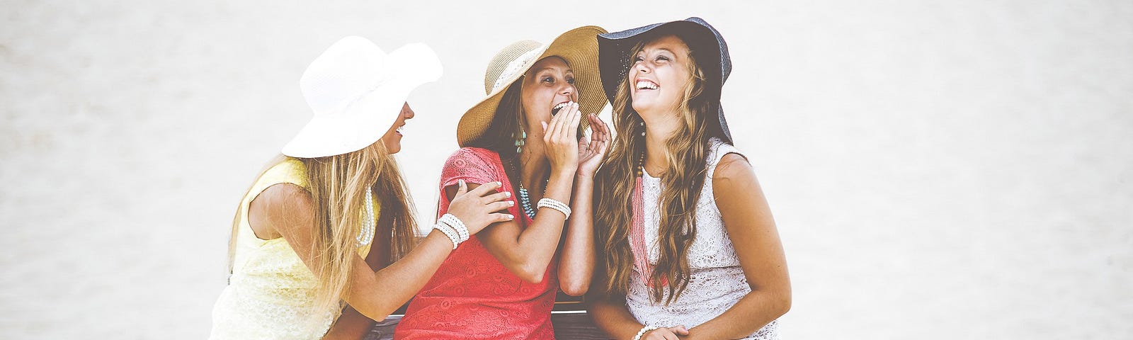3 women sitting on a bench on the beach talking and laughing