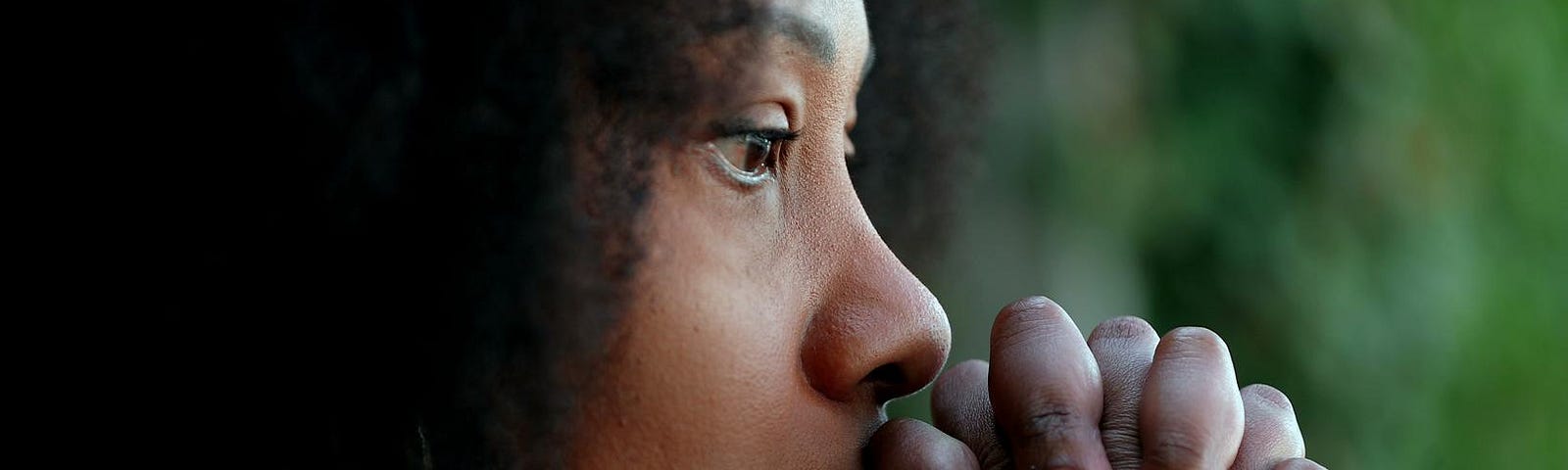 Close-up of a woman’s face with praying hands covering her mouth.