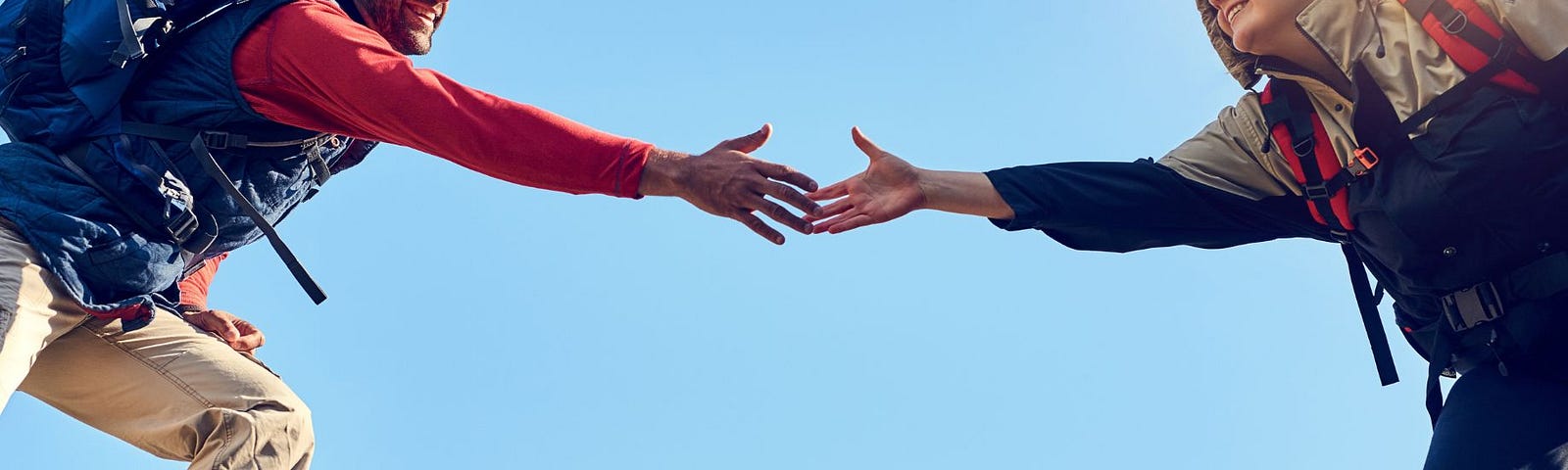 Man in hiking gear reaching out to grasp the hand of a woman about to cross a dangerous crevasse.