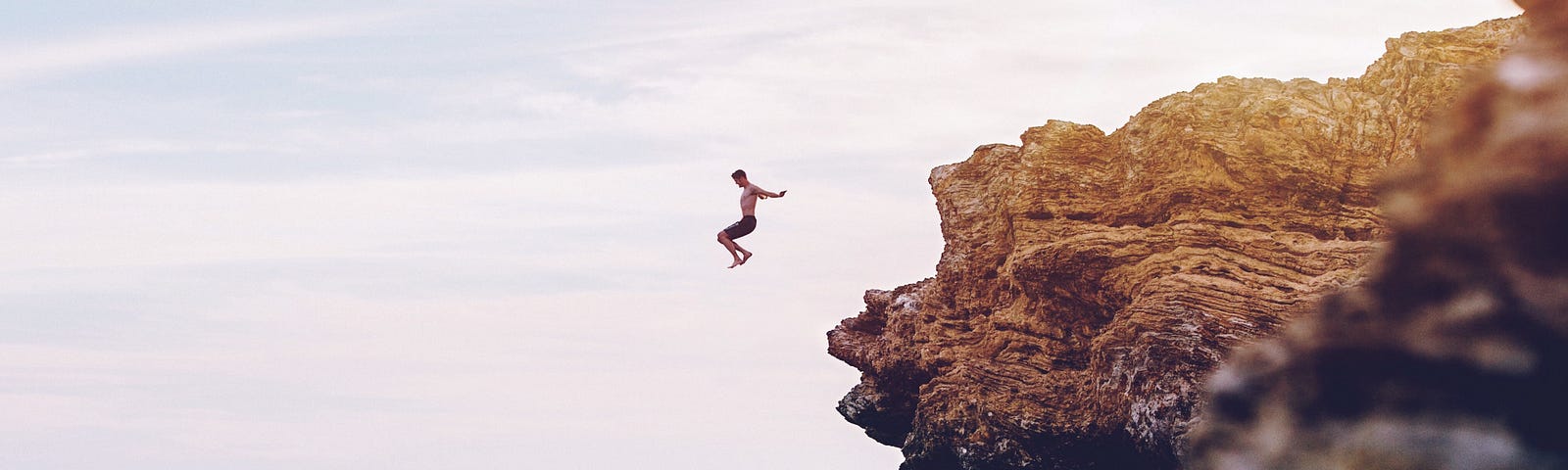 a brave man jumps from a tall cliff into the ocean