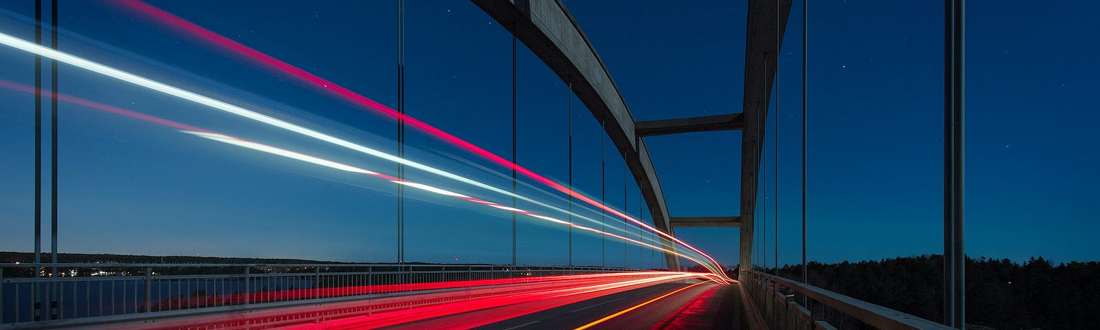 Bright lines of light accelerate across a bridge at night.