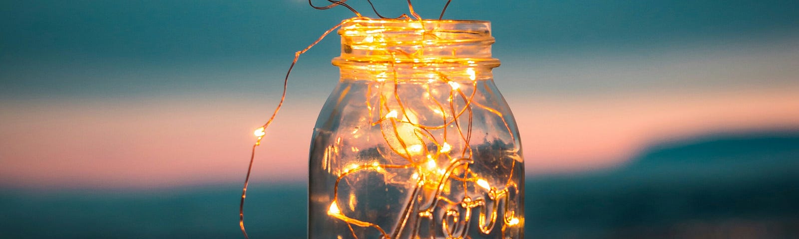 Golden lights on wire in a jar with blue and pink sky behind.