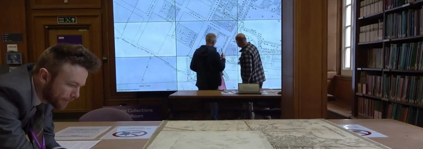 Three researchers looking at maps using a visualiser screen in the Special Collections Map Room at the Main Library, University of Manchester.