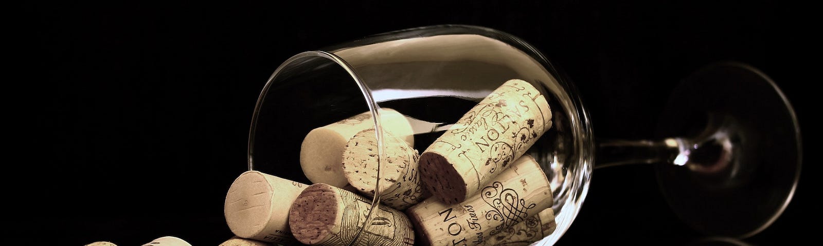A clean wineglass laying on its side with a dozen corks spilling out, photographed against a black background