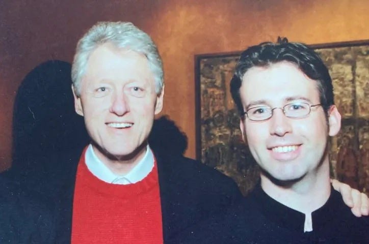 Former President Bill Clinton in a blue lazer and red sweater vest stands next to the author in a waiter uniform
