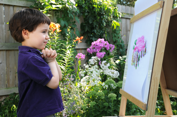 Young boy admiring his painting of a flower near him in the garden