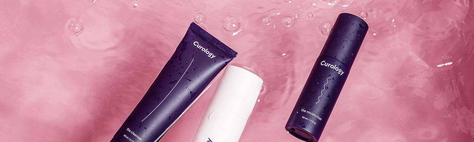 The Curology skincare set — the cleanser, moisturizer, and custom superbottle — against a pink backdrop