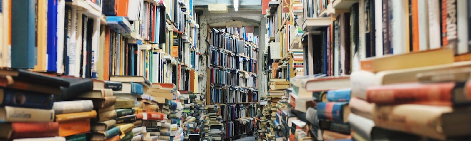 A library or bookstore with stacks of old books in messy piles.