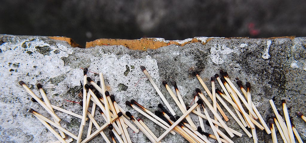 A pile of burnt-out matches on a piece of concrete.