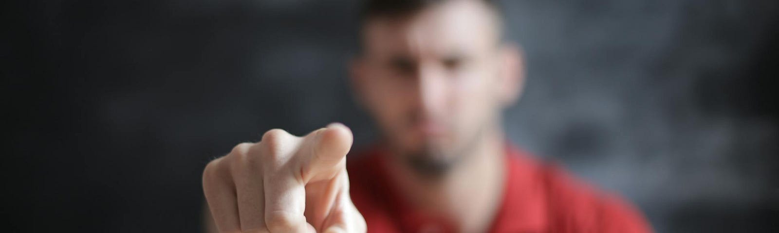 A man pointing at the camera. The man’s face and body are out of focus, but his finger pointing at you is perfectly in focus.