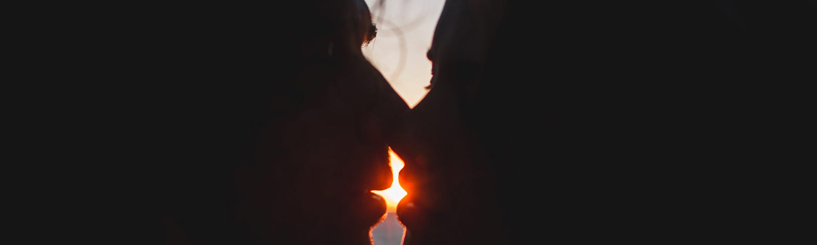 Man and woman kiss with the setting sun in the background