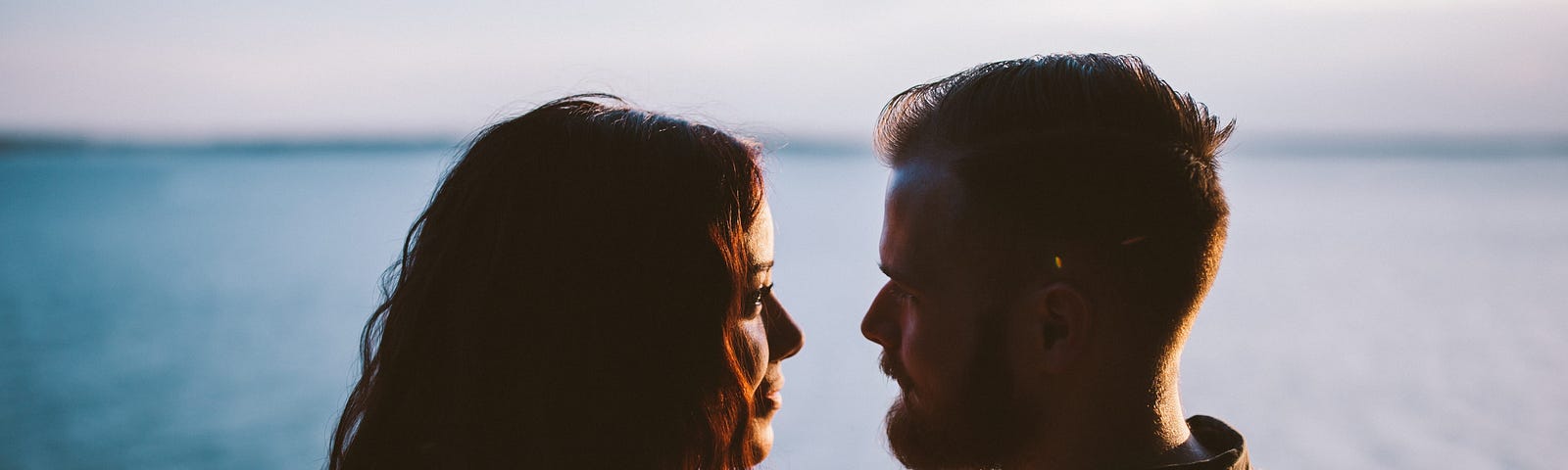 A man and a woman look at each other in front of a large body of water