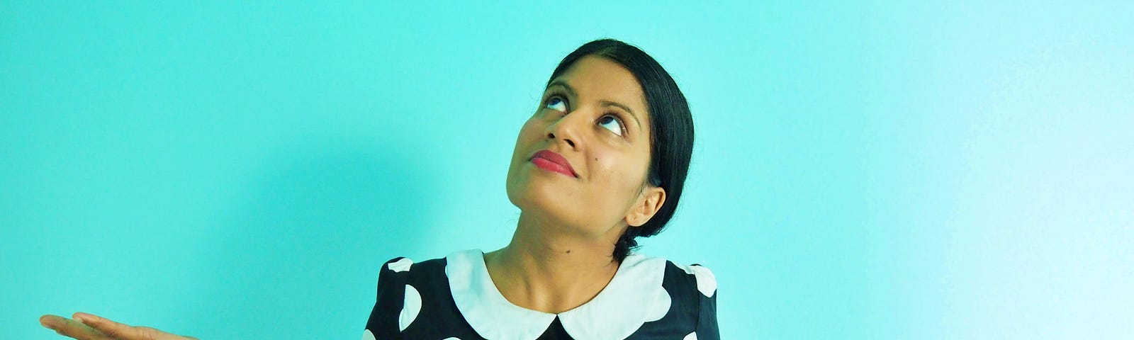 A girl in a polka dot dress looking up with her hands out in a questioning shrug