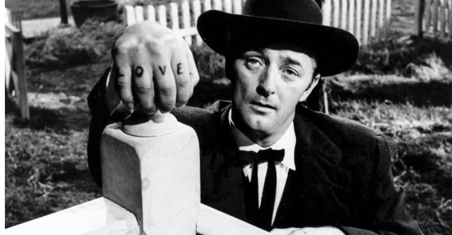 Robert Mitchum as Harry Powell in Night of the Hunter, posed with his hand on a newel post to show his L-O-V-E knuckle tattoos.