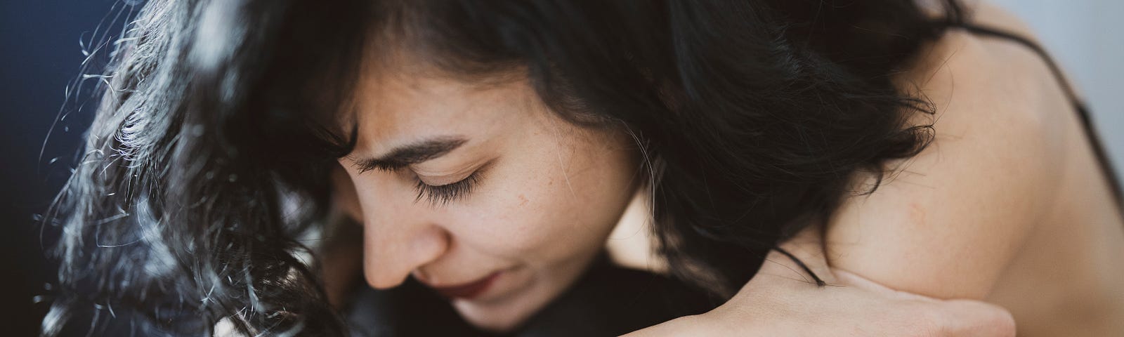 A young woman with a sad expression on her face hugging herself tightly.