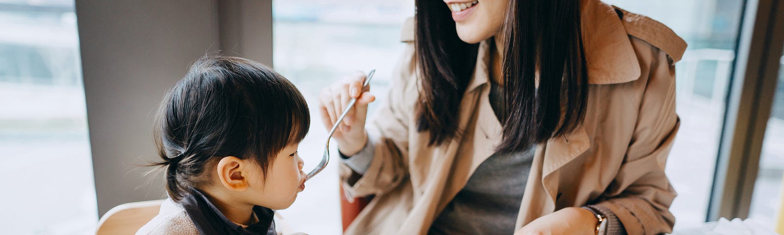 Mother and little daughter sharing a piece of cake in the cafe, both of them are smiling joyfully