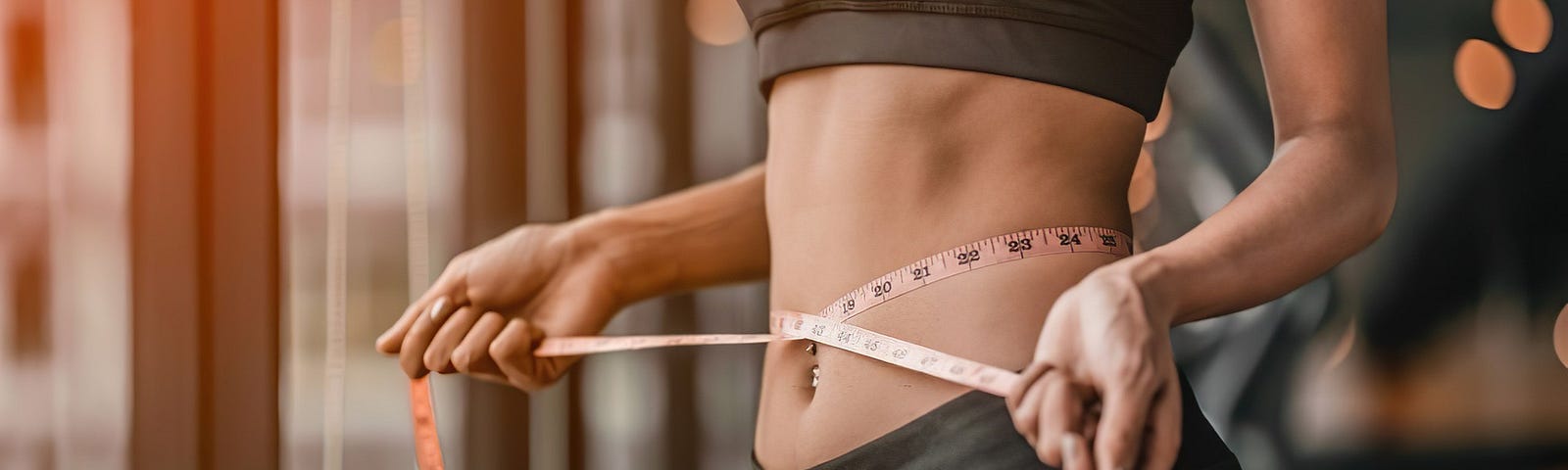 A thin woman in gym clothes is measuring her waistline.