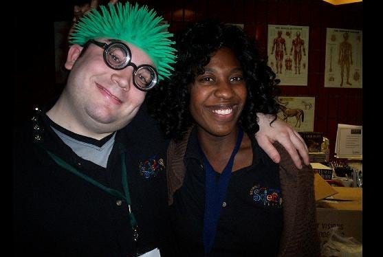man with green hair (wig?) smiles with arm around beautiful woman