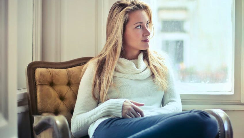 A woman with long blonde hair wearing a white sweater, with an amused look on her face.