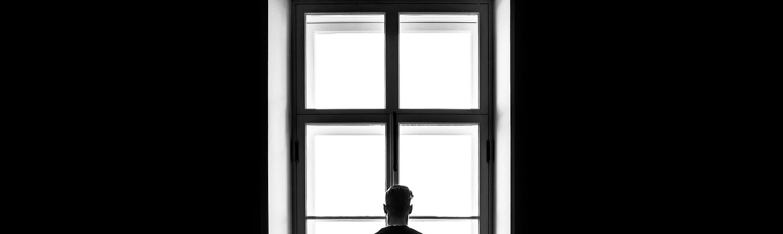 A man looks out the window, in sillouette