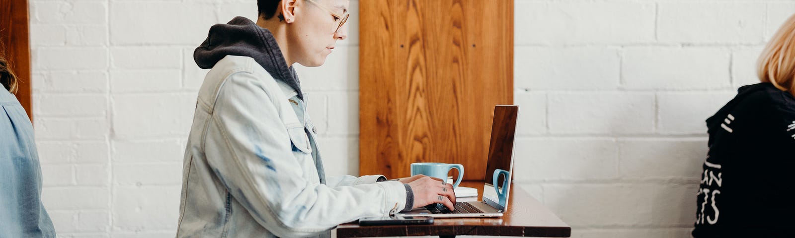 Person sits in a coffee shop, typing on their laptop.