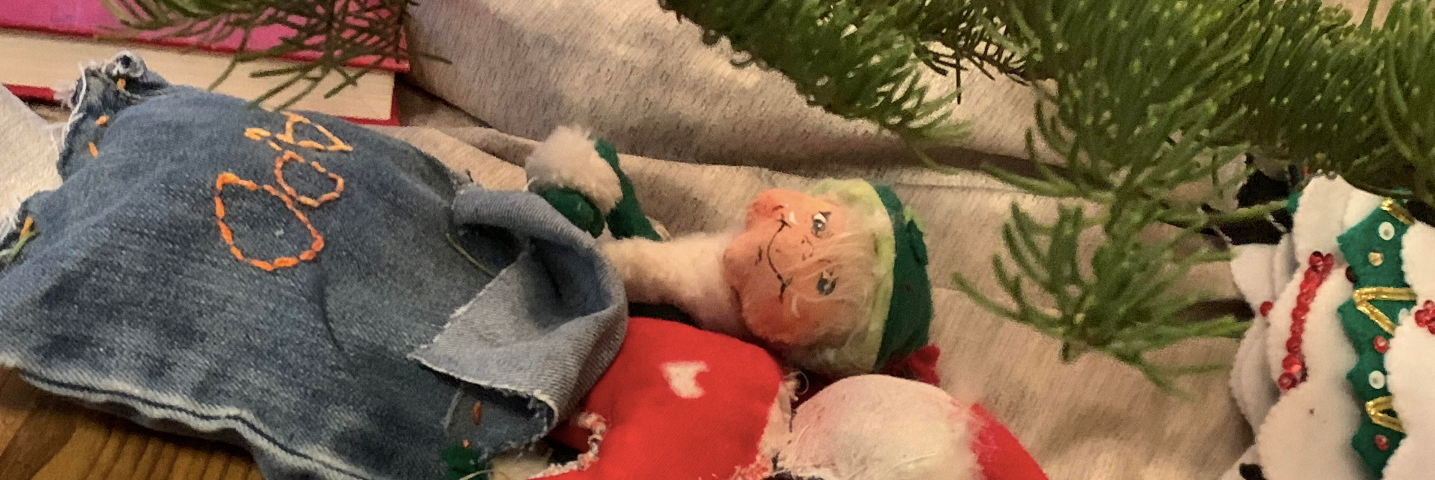 A store bought elf with a child-made elf in a child-made sleeping bag with a child-made pillow under the Christmas tree