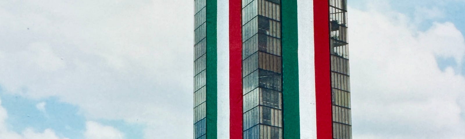 Photo of building in Mexico City, all glass, drapped with two green, white, red banners lengthwise, 25 stories long.