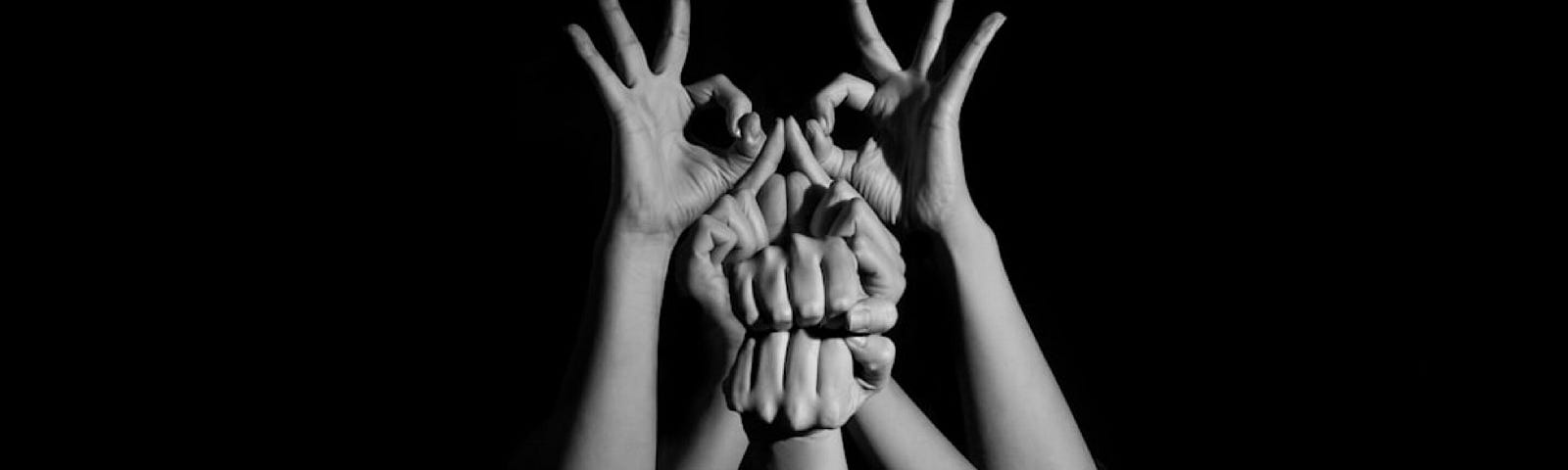 A group of hands reaching up in the air, forming different shapes with the fingers. A black and white photo
