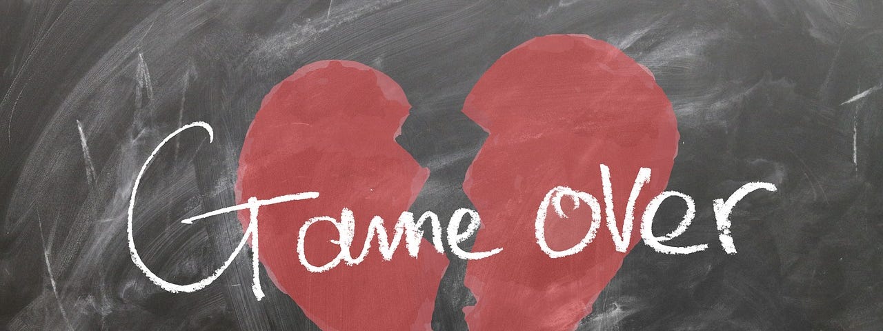 A red heart broken in two drawn on a blackboard in chalk and written over the top in white chalk is the words ‘Game Over’.